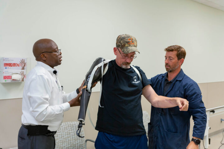 Patient with clinicians putting on a custom arm prosthetic