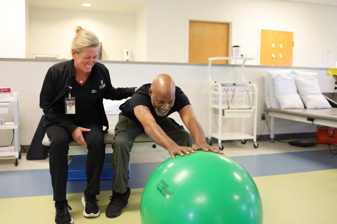 Outpatient therapy with patient, Michael Johnson, stretching with an exercise ball with the support of a therapist