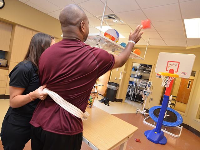 Patient tosses a bean bag with the support of a therapist